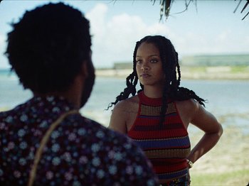 Movie still from “Guava Island” (2019), directed by Hiro Murai – A woman with dreads standing next to another woman; Medium shot, Over the shoulder angle