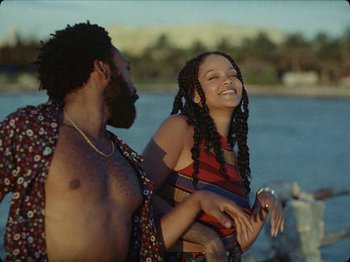 Movie still from “Guava Island” (2019), directed by Hiro Murai – A man standing next to a woman with long braids; Medium shot, Low angle