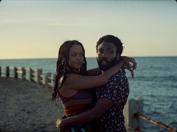 Movie still from “Guava Island” (2019), directed by Hiro Murai – A man and a woman hugging on the beach; Medium shot, Over the shoulder angle