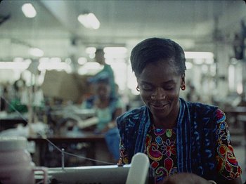 Movie still from “Guava Island” (2019), directed by Hiro Murai – A woman is smiling while working on a computer; Medium shot, Low angle
