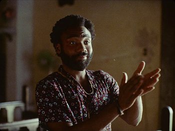 Movie still from “Guava Island” (2019), directed by Hiro Murai – A man claps his hands while standing in front of a mirror; Close Up shot, Over the shoulder angle