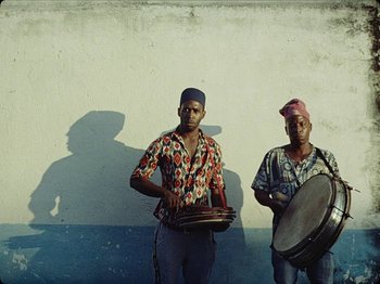 Movie still from “Guava Island” (2019), directed by Hiro Murai – Two men are standing next to each other; Medium shot, Low angle