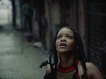 Movie still from “Guava Island” (2019), directed by Hiro Murai – A young woman with long black braids looking up; Close Up shot, Overhead angle