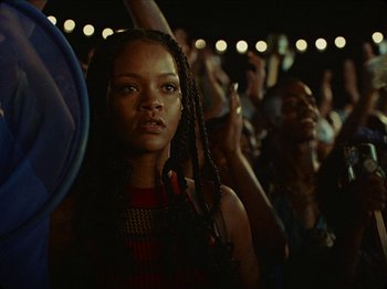 Movie still from “Guava Island” (2019), directed by Hiro Murai – A person at an event; Close Up shot, Over the shoulder angle