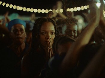 Movie still from “Guava Island” (2019), directed by Hiro Murai – A group of people standing in front of a crowd at night; Close Up shot, Low angle