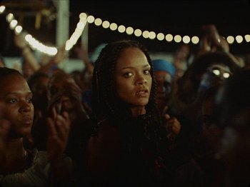 Movie still from “Guava Island” (2019), directed by Hiro Murai – A crowd of people standing in a room; Close Up shot, Over the shoulder angle