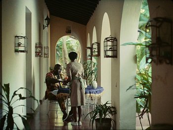 Movie still from “Guava Island” (2019), directed by Hiro Murai – Two women are sitting at a table in an archway; Wide shot, High angle