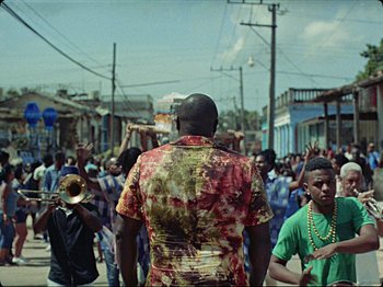 Movie still from “Guava Island” (2019), directed by Hiro Murai – A group of people walking down a street; Extreme Wide shot, Over the shoulder angle