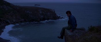 Movie still from “I Know What You Did Last Summer” (1997), directed by Jim Gillespie – A man sitting on the edge of a cliff by the ocean; Wide shot, High angle