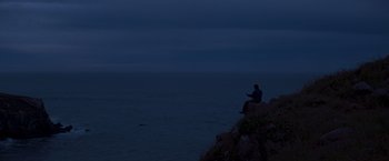 Movie still from “I Know What You Did Last Summer” (1997), directed by Jim Gillespie – A man sitting on top of a cliff looking at the ocean; Extreme Wide shot, High angle