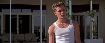 Movie still from “I Know What You Did Last Summer” (1997), directed by Jim Gillespie – A man in a white tank top is standing in front of a house; Medium shot, Low angle