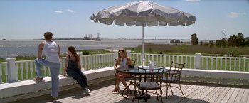 Movie still from “I Know What You Did Last Summer” (1997), directed by Jim Gillespie – A woman sitting at a table under an umbrella; Wide shot, High angle
