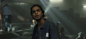 Movie still from “Gully Boy” (2019), directed by Zoya Akhtar – A man with long black hair standing in a dark room; Close Up shot, Low angle