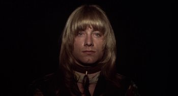 Movie still from “Hair” (1979), directed by Milos Forman – A man with long blonde hair wearing a neck tie; Close Up shot, Low angle
