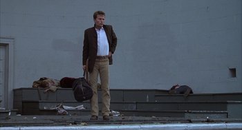 Movie still from “Hair” (1979), directed by Milos Forman – A man standing on the side of the street holding a bag; Wide shot, Low angle