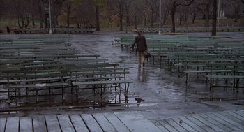 Movie still from “Hair” (1979), directed by Milos Forman – A man walking in the rain near a lot of benches; Wide shot, High angle