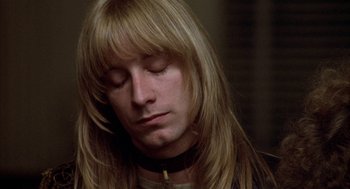 Movie still from “Hair” (1979), directed by Milos Forman – A man with long blonde hair wearing a black collar; Close Up shot, High angle