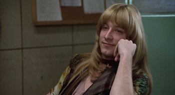 Movie still from “Hair” (1979), directed by Milos Forman – A man with long blonde hair sitting in front of a brick wall; Close Up shot, Low angle