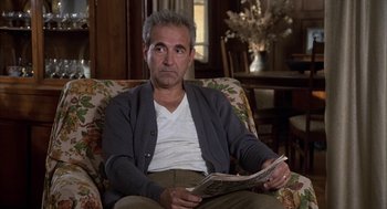 Movie still from “Hair” (1979), directed by Milos Forman – A man sitting in a chair reading a newspaper; Medium shot, High angle