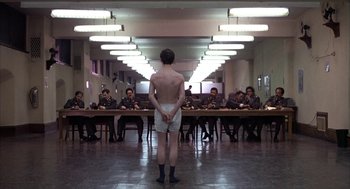 Movie still from “Hair” (1979), directed by Milos Forman – A man standing in front of a group of people; Wide shot, High angle