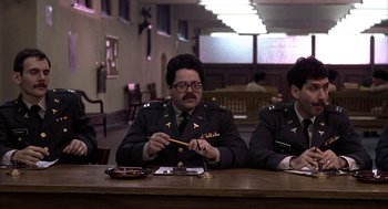 Movie still from “Hair” (1979), directed by Milos Forman – A man sitting at a table with a pencil in front of him; Medium shot, High angle