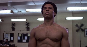 Movie still from “Hair” (1979), directed by Milos Forman – A man with no shirt is standing in a gym; Close Up shot, Low angle