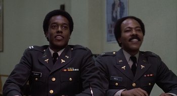 Movie still from “Hair” (1979), directed by Milos Forman – A couple of men sitting next to each other in uniforms; Medium shot, Low angle