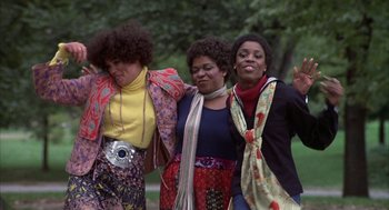 Movie still from “Hair” (1979), directed by Milos Forman – A group of women standing next to each other in a park; Medium shot, Low angle