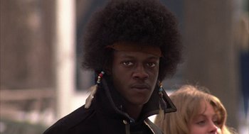 Movie still from “Hair” (1979), directed by Milos Forman – A man with a black jacket with feathers on his head; Close Up shot, Low angle