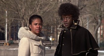 Movie still from “Hair” (1979), directed by Milos Forman – A woman standing next to a man wearing a jacket; Medium shot, Low angle