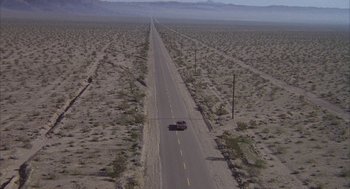 Movie still from “Hair” (1979), directed by Milos Forman – An aerial view of a car driving down a desert road; Extreme Wide shot, High angle