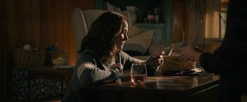 Movie still from “Halloween Ends” (2022), directed by David Gordon Green – A woman sitting at a table with a glass of wine; Medium shot, Over the shoulder angle