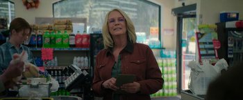 Movie still from “Halloween Ends” (2022), directed by David Gordon Green – A woman holding a cell phone while standing in a store; Medium shot, Low angle