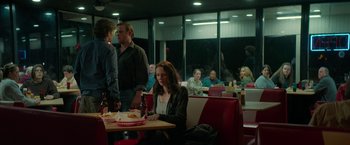 Movie still from “Halloween Ends” (2022), directed by David Gordon Green – A woman sitting at a table in front of a group of people; Wide shot, Over the shoulder angle