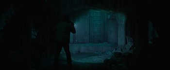 Movie still from “Halloween Ends” (2022), directed by David Gordon Green – A man standing in a dark room with a flashlight; Wide shot, Low angle