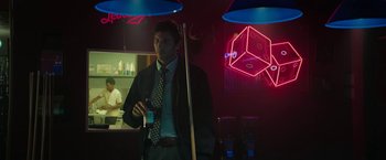 Movie still from “Halloween Ends” (2022), directed by David Gordon Green – A man standing in a room next to a neon sign; Medium shot, Over the shoulder angle