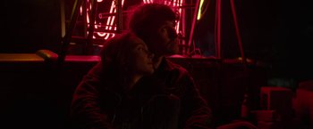 Movie still from “Halloween Ends” (2022), directed by David Gordon Green – A man and a woman sitting next to each other in front of neon lights; Medium shot, Low angle