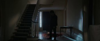 Movie still from “Halloween Ends” (2022), directed by David Gordon Green – A man standing in the dark in front of a staircase; Wide shot, Low angle