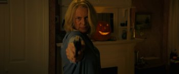 Movie still from “Halloween Ends” (2022), directed by David Gordon Green – A woman holding a gun in front of an orange pumpkin; Close Up shot, Over the shoulder angle