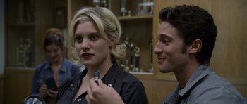 Movie still from “Halloween: Resurrection” (2002), directed by Rick Rosenthal – A woman is holding a cell phone in front of a man; Close Up shot, Over the shoulder angle