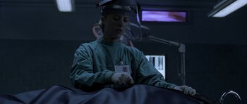 Movie still from “Halloween: Resurrection” (2002), directed by Rick Rosenthal – A man wearing a surgical mask is sitting on a bed; Medium shot, Low angle