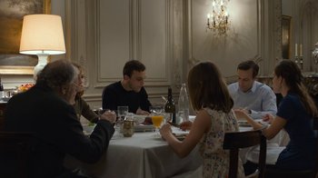 Movie still from “Happy End” (2017), directed by Michael Haneke – A group of people sitting around a table eating food; Medium shot, Over the shoulder angle