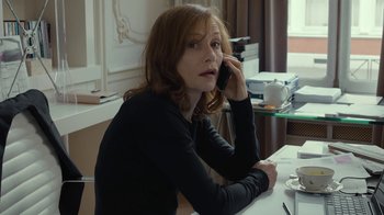 Movie still from “Happy End” (2017), directed by Michael Haneke – A woman sitting at a table talking on a phone; Medium shot, High angle