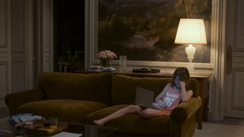 Movie still from “Happy End” (2017), directed by Michael Haneke – A little girl sitting on top of a brown couch with a laptop; Medium shot, High angle