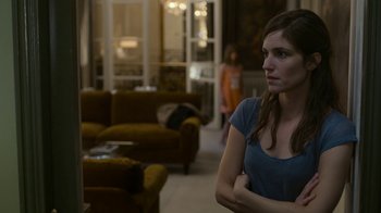Movie still from “Happy End” (2017), directed by Michael Haneke – A woman standing in front of a couch in a living room; Medium shot, Over the shoulder angle