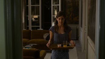 Movie still from “Happy End” (2017), directed by Michael Haneke – A woman is holding a tray of food in a living room; Medium shot, Over the shoulder angle