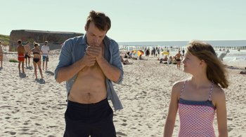 Movie still from “Happy End” (2017), directed by Michael Haneke – A man and a woman standing on a sandy beach; Medium shot, Over the shoulder angle