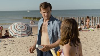 Movie still from “Happy End” (2017), directed by Michael Haneke – A man and a woman are on the beach; Medium shot, Over the shoulder angle