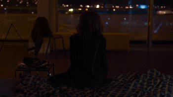 Movie still from “Happy End” (2017), directed by Michael Haneke – A woman sitting on a bed looking out a window at night; Medium shot, High angle