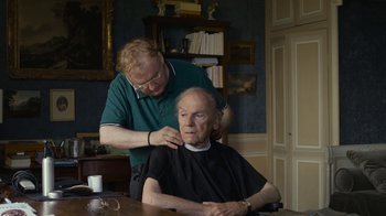Movie still from “Happy End” (2017), directed by Michael Haneke – An older man getting his hair cut by a barber; Medium shot, Over the shoulder angle
